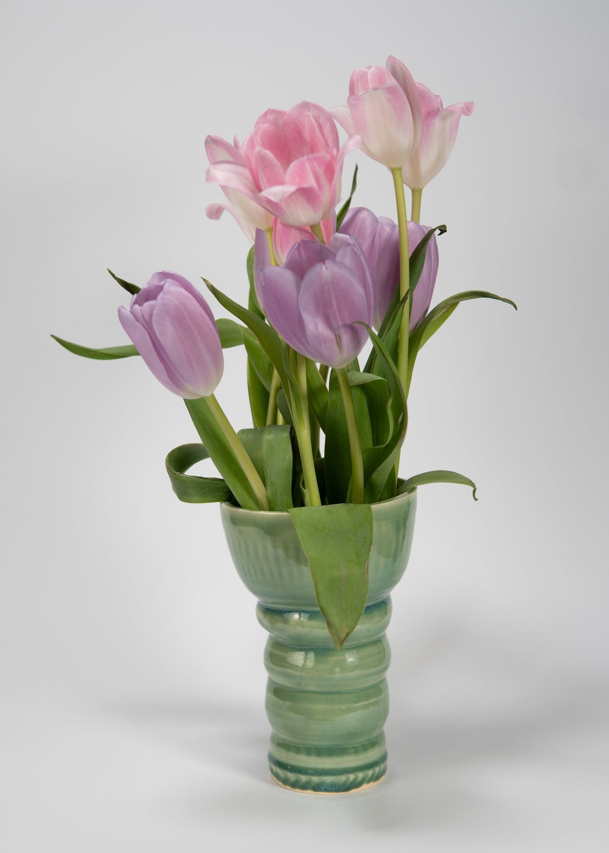 Green vase with pink and purple tulips on a white background
